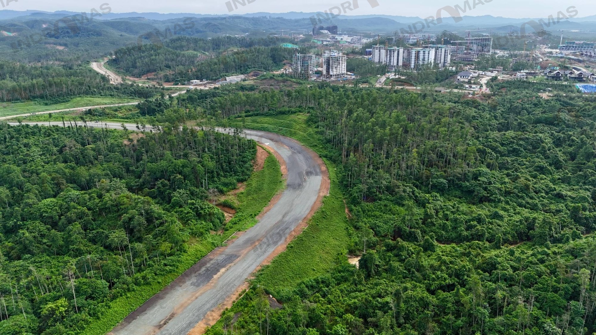 Aerial view of a road with revegetated green slopes winding through forest towards Nusantara, Indonesia's new capital