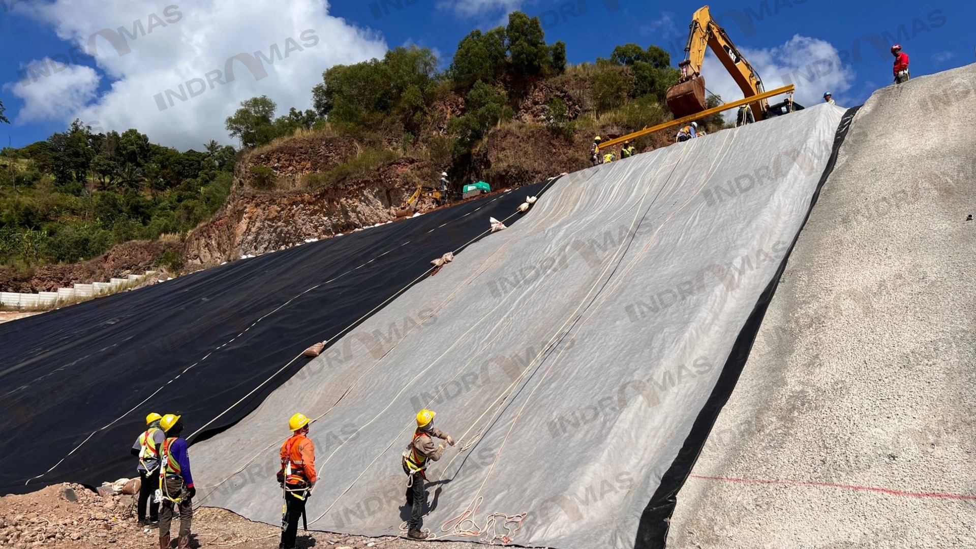 Indramas crew deploying geotextile and HDPE geomembrane down a steep slope with rope access